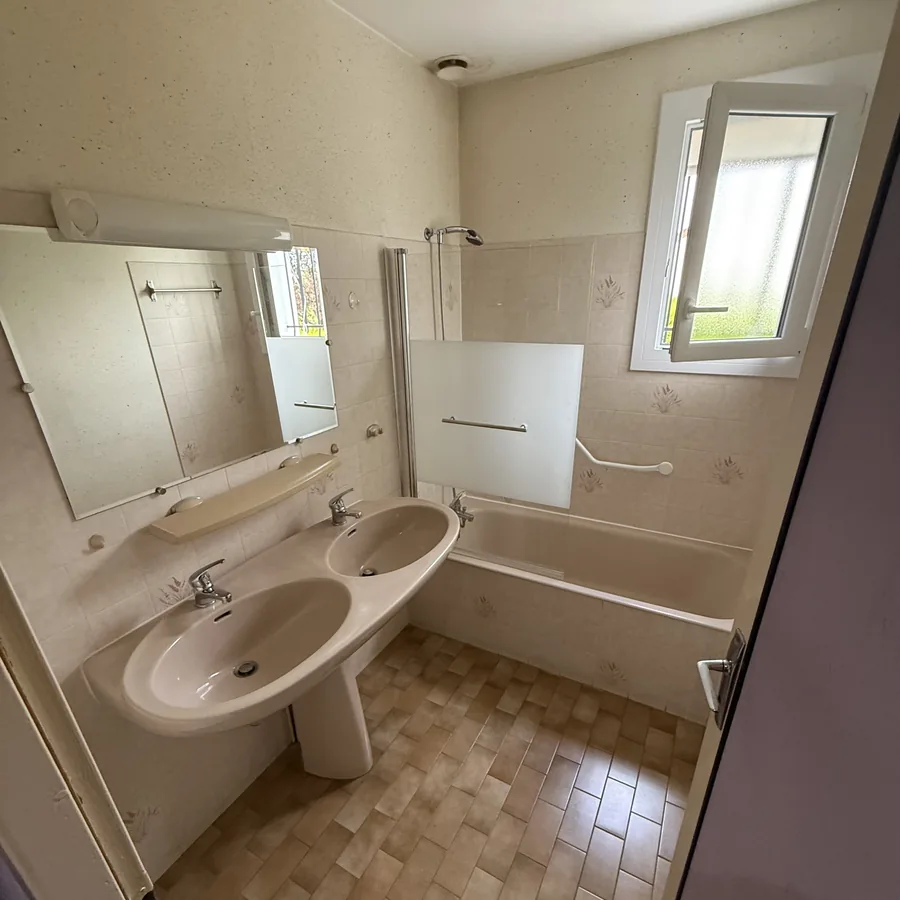 Salle de bains avant rénovation : baignoire, double vasque et carrelage beige d'origine